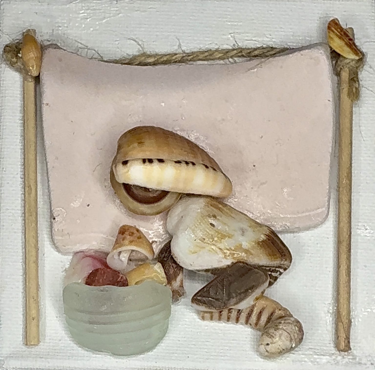 Washing Day is a mixed media collage piece on canvas made from sea shells, sea glass & beach detritus depicting a domestic scene where a woman bends to her laundry basket while hanging out her wet clothes clothes to dry in the sun. A pink quilt is already draped on the line.